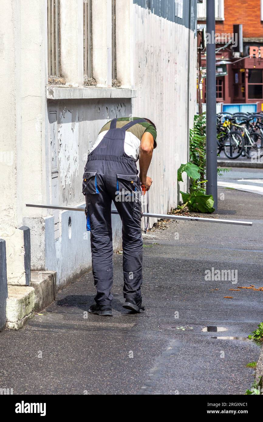 Männlicher Arbeiter, der den Metallwinkel mit der Säge falsch mit dem Knie als Stütze schneidet - Paris, Frankreich. Stockfoto