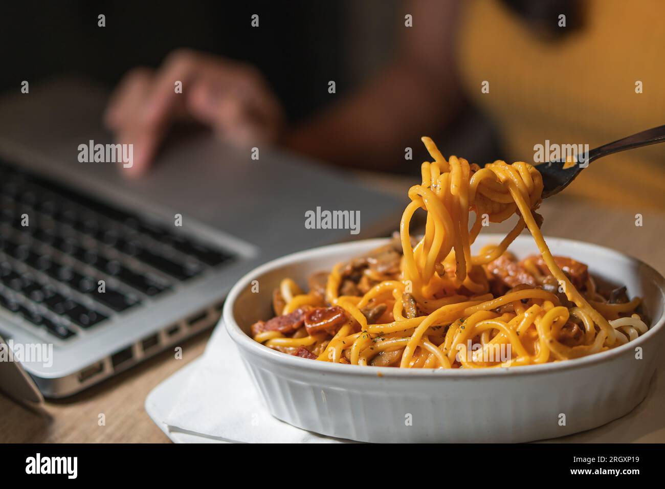 Spaghetti essen, während Sie zu Hause an einem Laptop arbeiten. Ungesundes Essen während Konferenzgespräch, Meeting. Stockfoto
