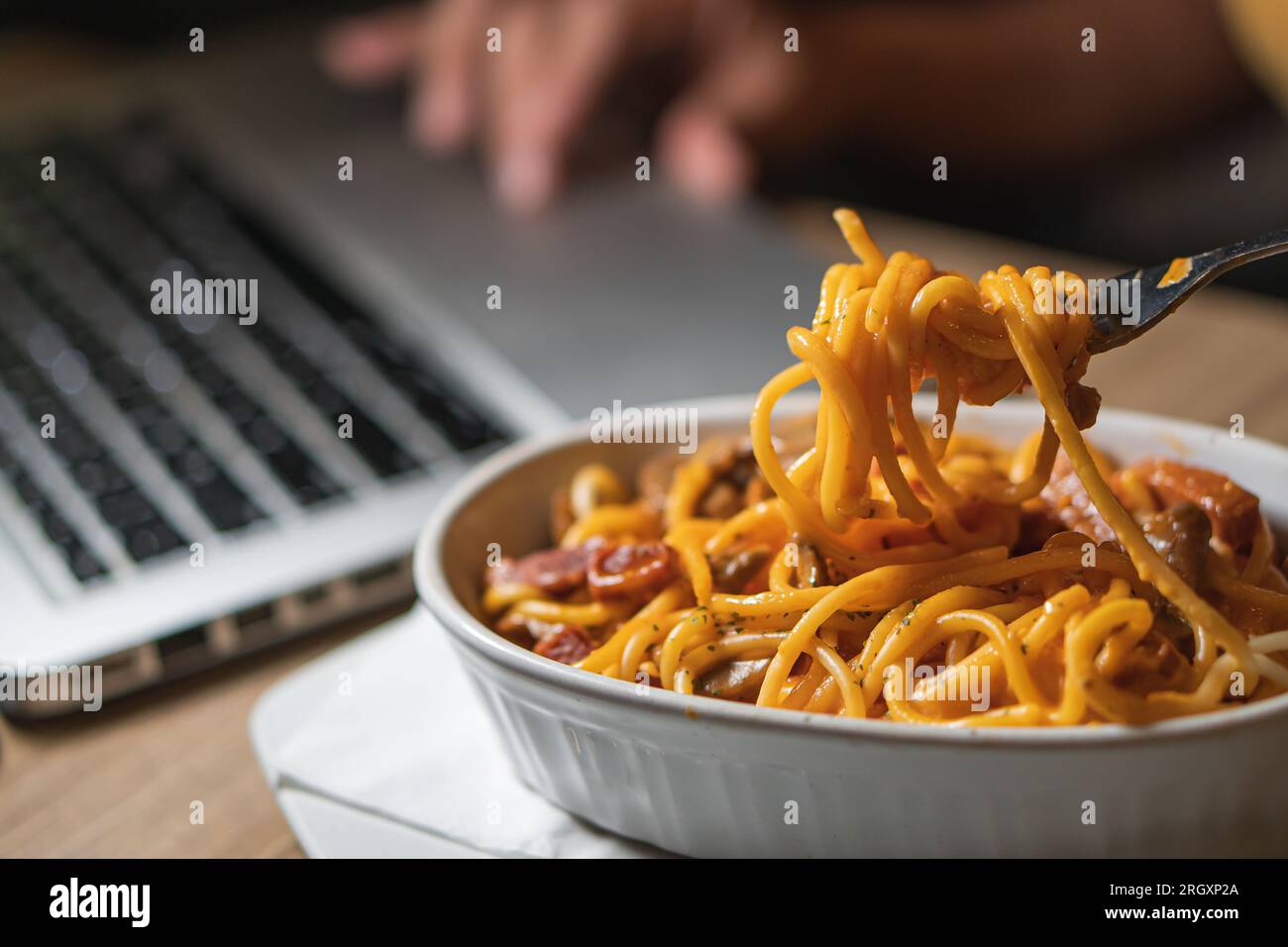 Spaghetti essen, während Sie zu Hause an einem Laptop arbeiten. Ungesundes Essen während Konferenzgespräch, Meeting. Stockfoto