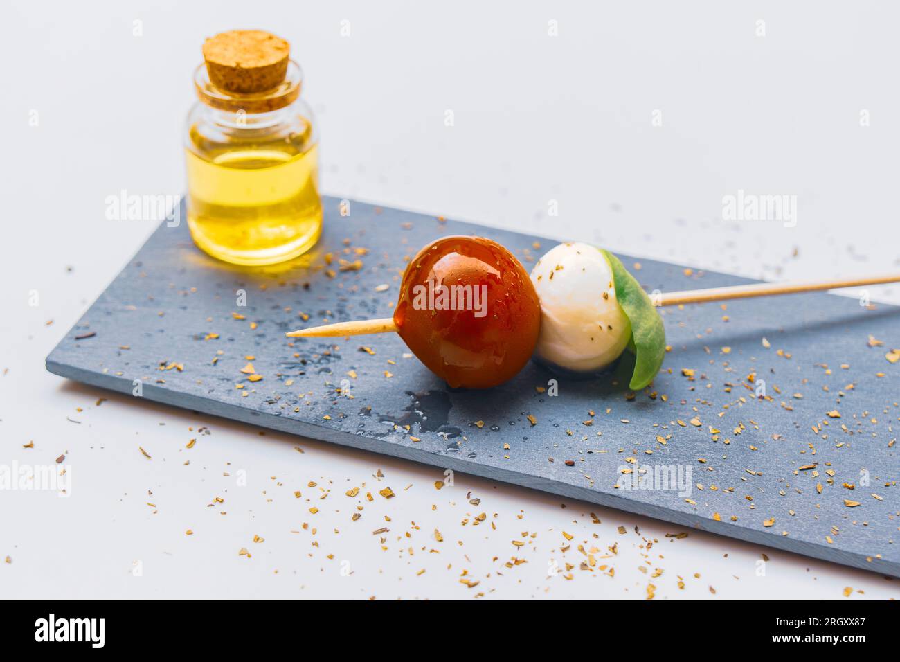 Kirschtomaten, Mozzarella-Käse und Basilikumblätter auf einem Spieß und einem Glas mit nativem Olivenöl extra. Stockfoto