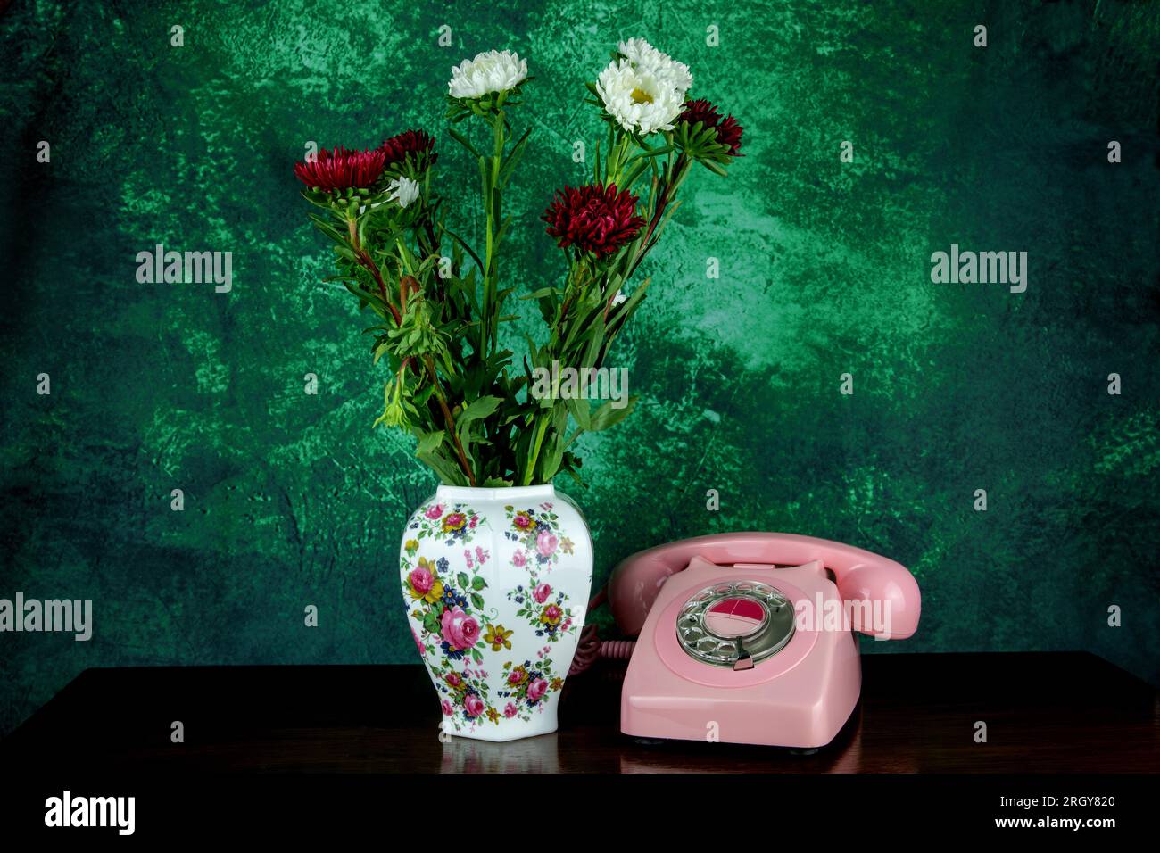 Telefon in Vintage-Pink mit Blumenvase auf einem polierten Holztisch Stockfoto