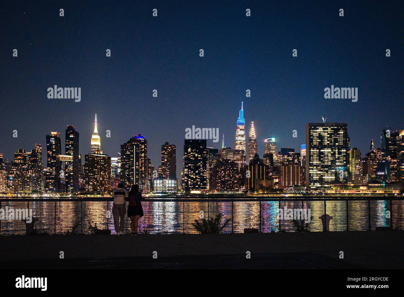 Verbindung zur Stadtlandschaft: Ein Paar genießt den Blick von Hunter's Point, Long Island City, während Manhattans Skyline die Nacht über dem East River erleuchtet Stockfoto