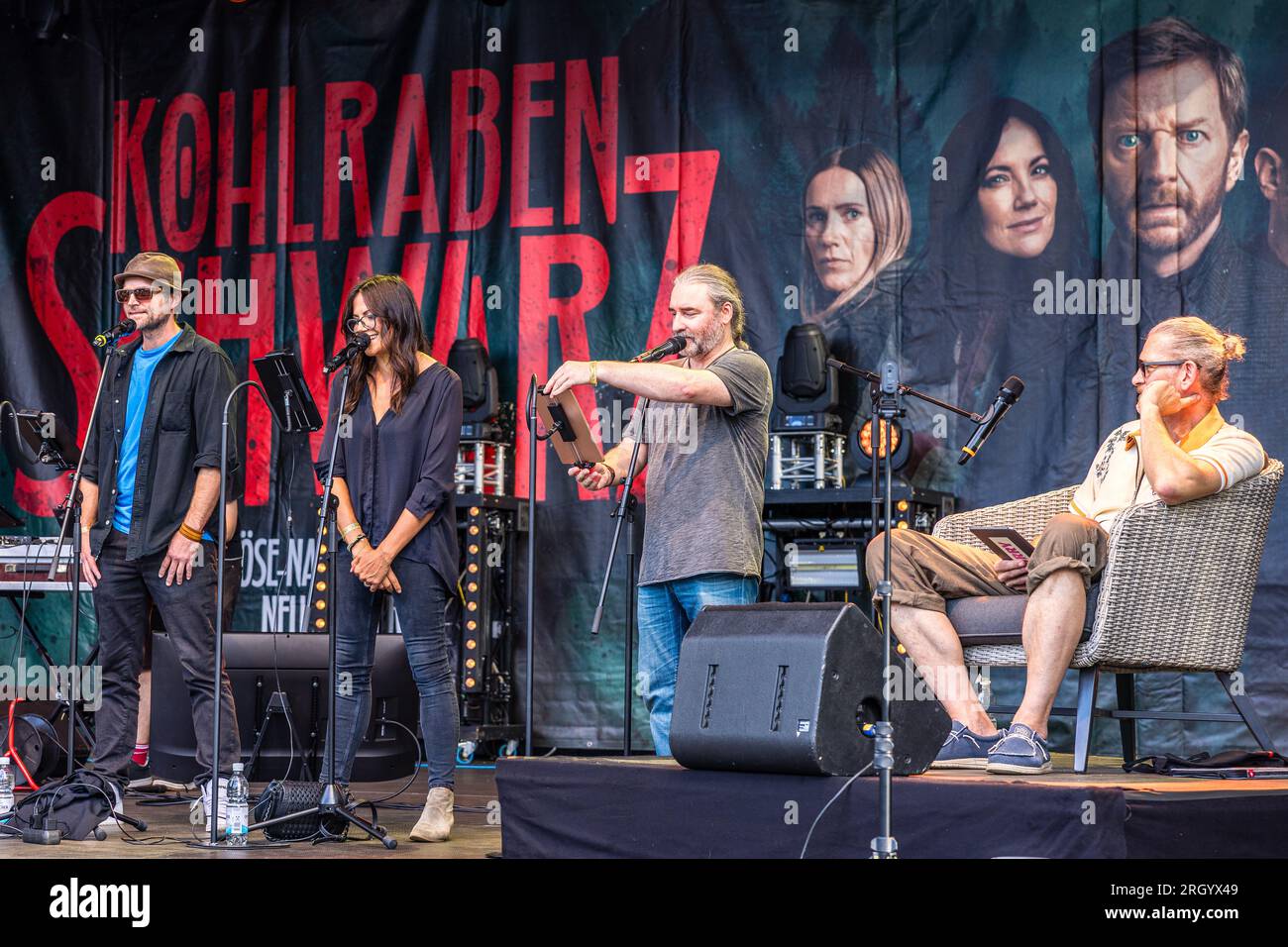 Cottbus, Deutschland. 12. Aug. 2023. Die Schauspieler Peter Ketnath (l) und Götz Otto (r), die Schauspielerin Bettina Zimmermann und der Autor Tommy Krappweis sind auf der Bühne für eine Live-Episode des Radioauftritts Kohlrabenschwarz beim Elbenwald Festival. Das Elbenwald Festival ist ein dreitägiges Treffen für Menschen jeden Alters, die Filme, Fantasie, Spiele, Konzerte und eine beliebige Kombination der oben genannten genießen. Die Organisatoren erwarten etwa 15.000 Besucher. Kredit: Frank Hammerschmidt/dpa/Alamy Live News Stockfoto