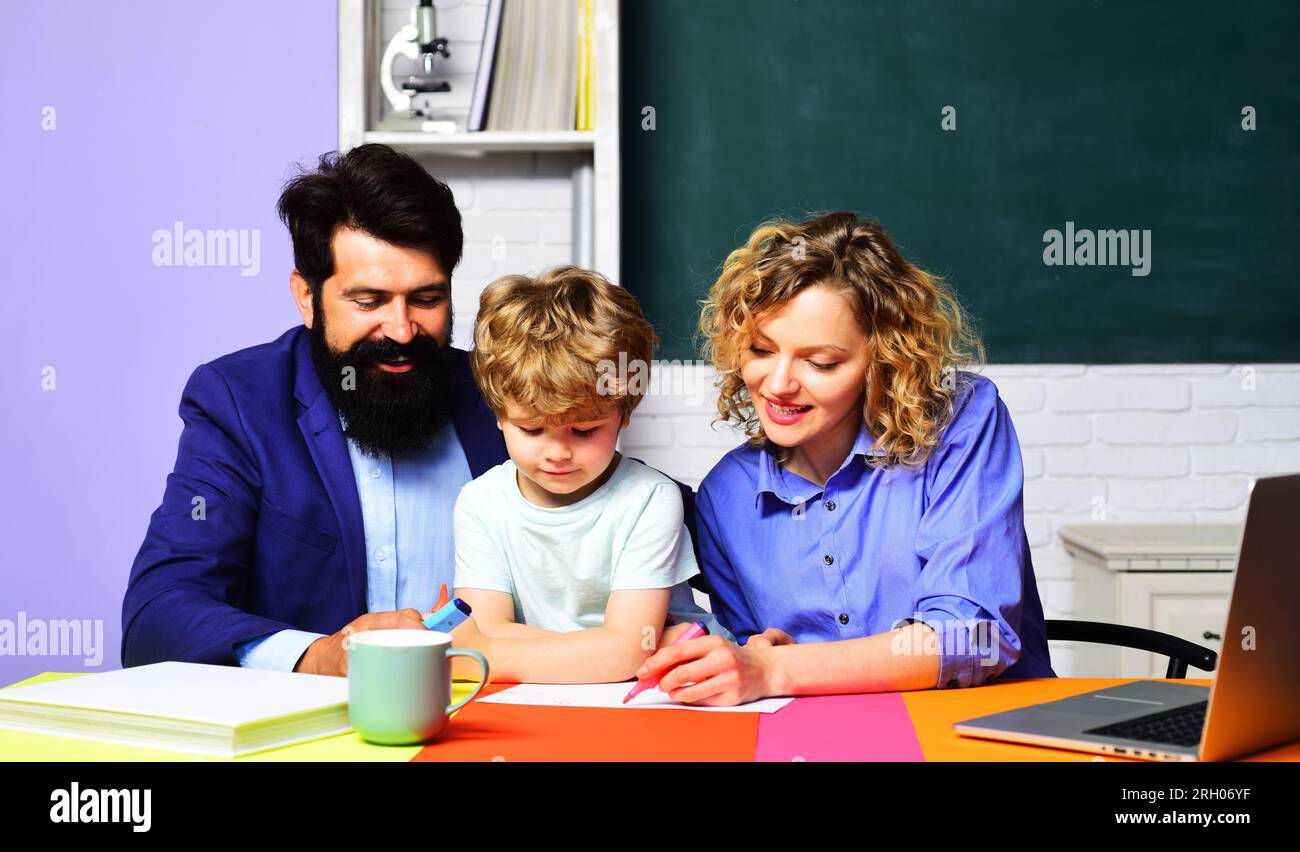 Lehrer helfen einem Jungen aus der Grundschule, Hausaufgaben zu machen. Schüler mit Eltern, die zusammen studieren. Kleine Kinderschülerin in der Grundschule Stockfoto