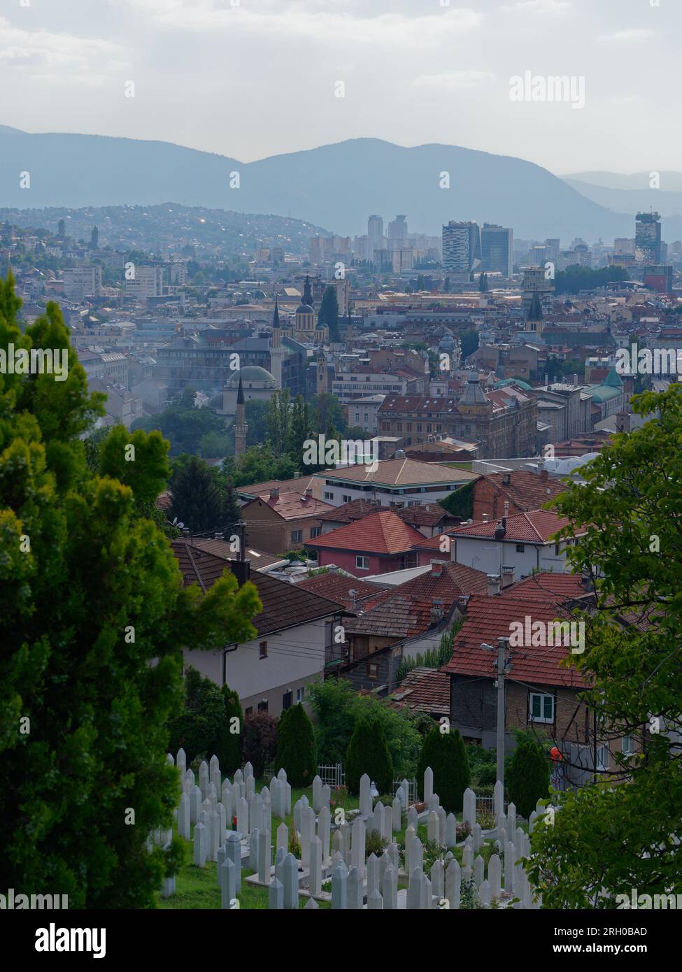 Erhöhter Blick über einen Friedhof und die Stadt Sarajevo mit modernen Hochhäusern und Bergen im Hintergrund, Bosnien und Herzegowina, 12. August 2023. Stockfoto