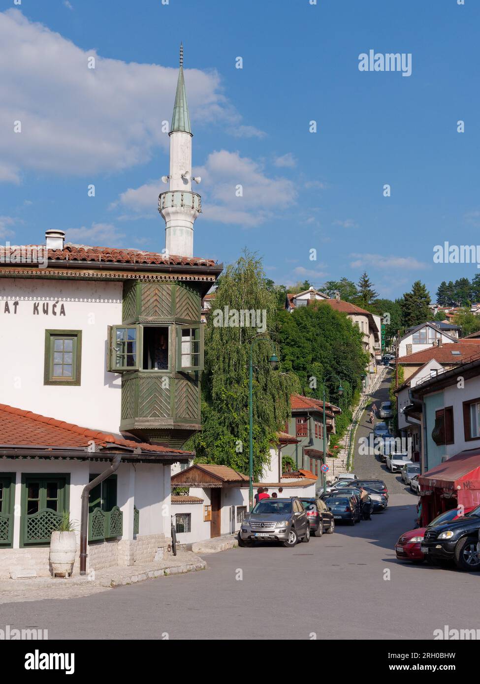 Restaurant Inat Kuca mit einem Minarett dahinter und einer steilen Straße voller Autos, die am 12. August 2023 in Sarajevo, Bosnien und Herzegowina, geparkt wurden. Stockfoto