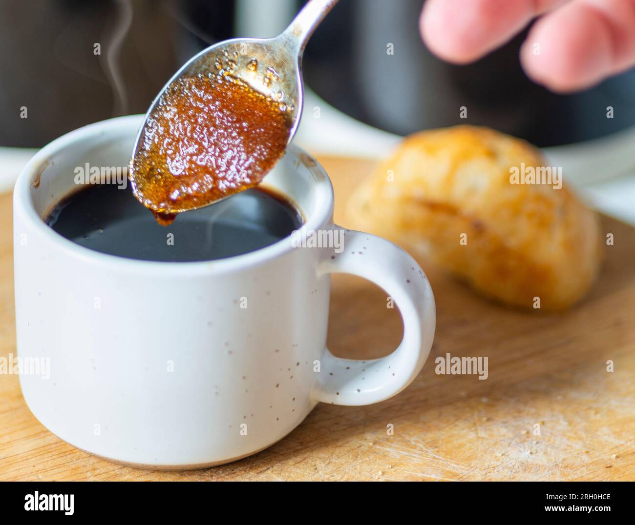 Braune Zuckerkörner ziehen den heißen Kaffee zu einer sirupen Konsistenz auf, bevor sie in einen frisch gebrühten schwarzen Espresso gerührt werden, der trinkfertig und heiß ist Stockfoto