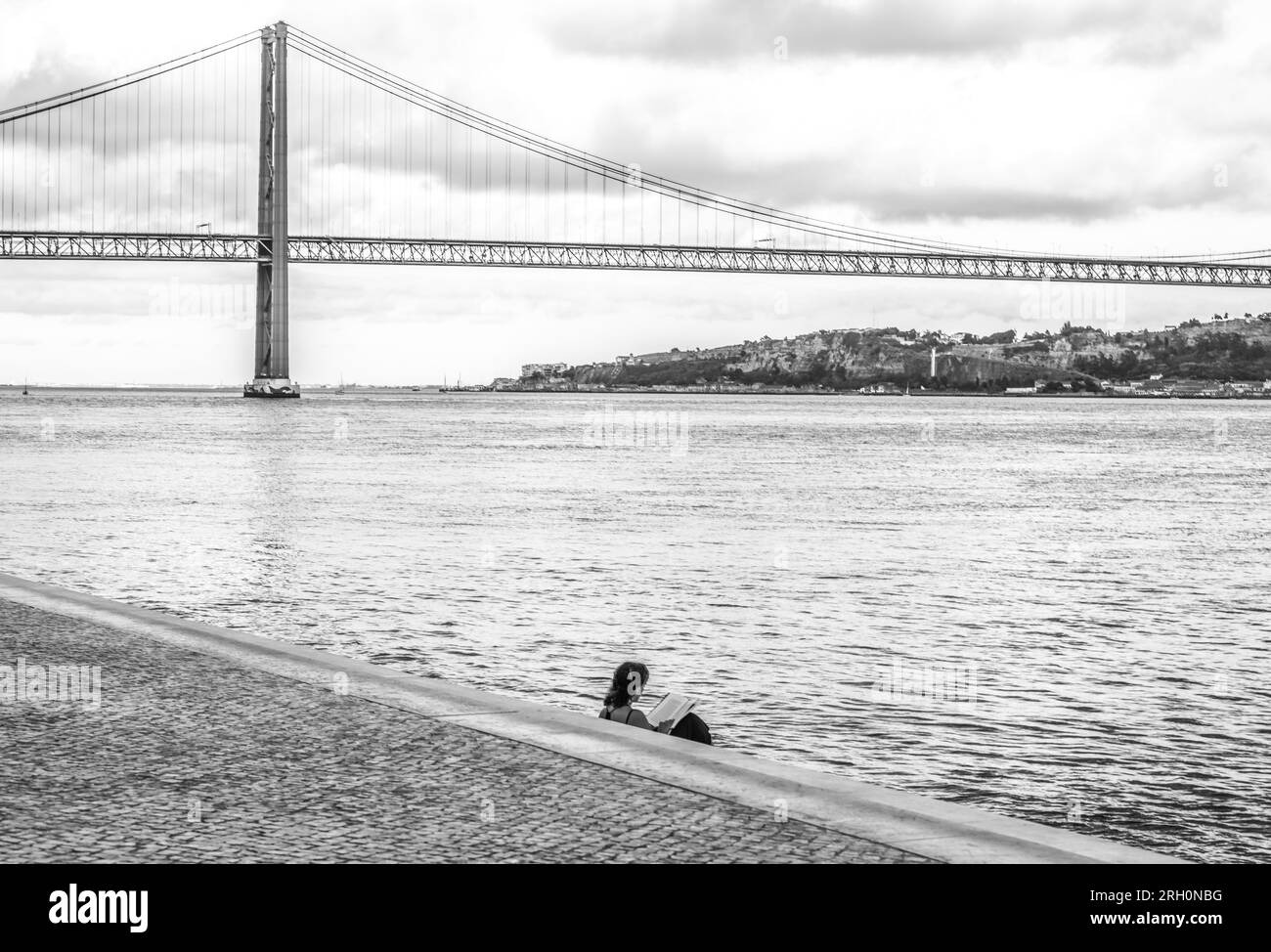 Lissabon, Portgugal. Frau, die am Targus-Fluss liegt. Berühmte Brücke Ponte 25 de Abril im Hintergrund. Stockfoto