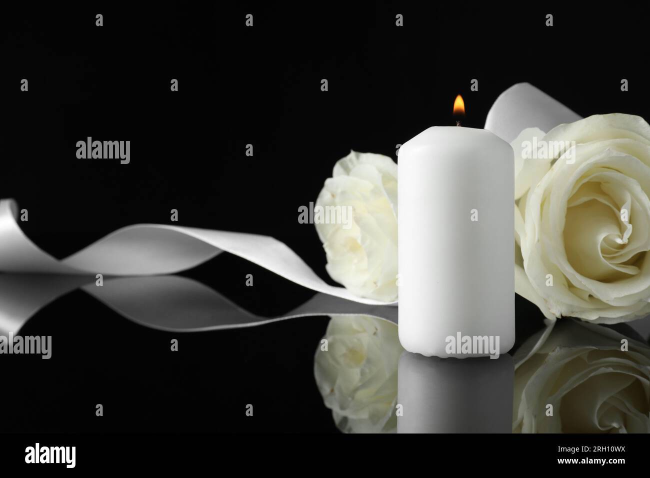 Brennende Kerze, weiße Rosen und Band auf schwarzer Spiegeloberfläche bei Dunkelheit, Nahaufnahme mit Platz für Text. Begräbnissymbole Stockfoto