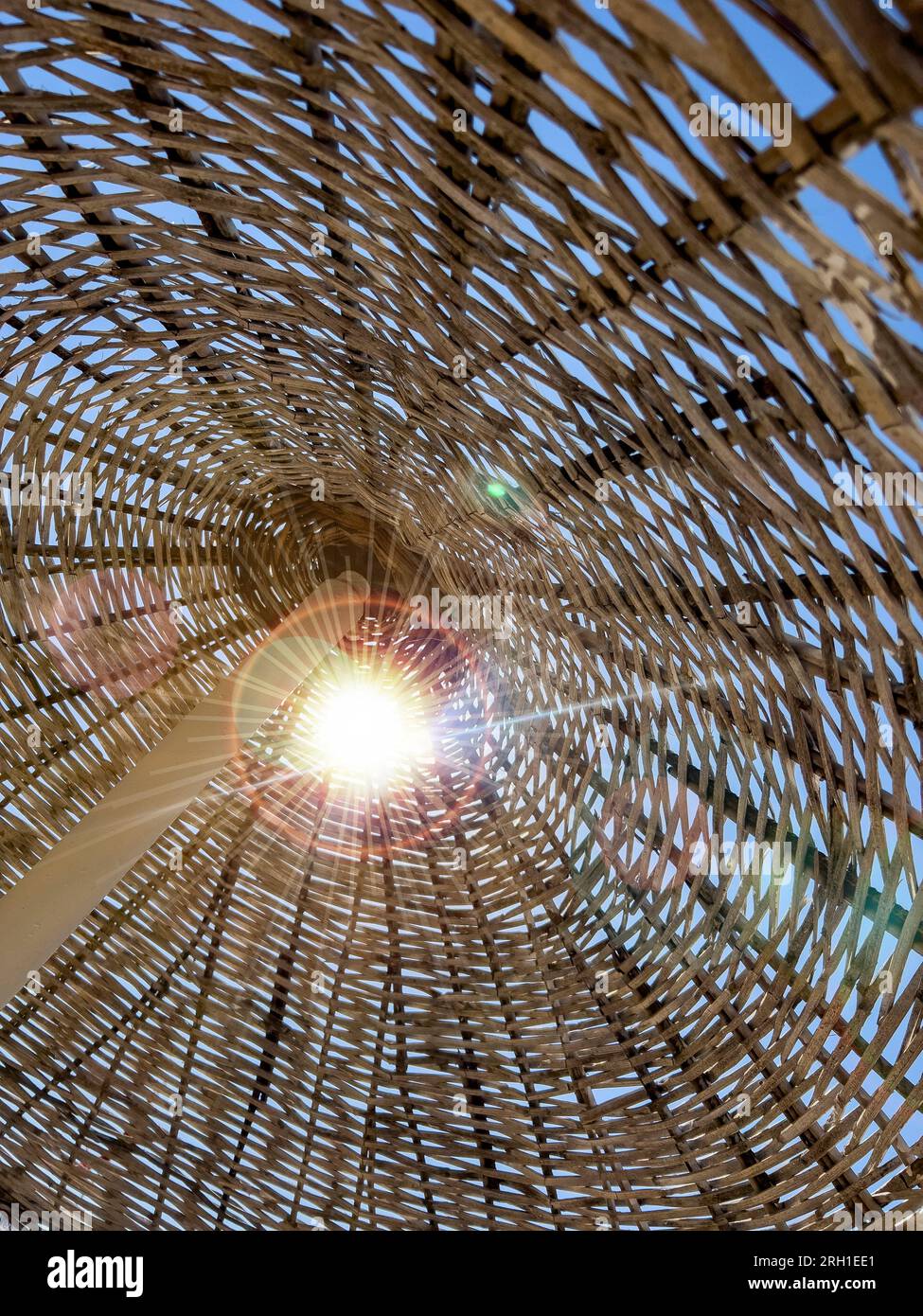 Strohstrukturierter Rattanschirm am Strand, vertikal. Sonnenstrahl fällt an sonnigen Tagen durch einen exotischen Sonnenschirm. Sommerspielhintergrund mit Kopierraum Stockfoto