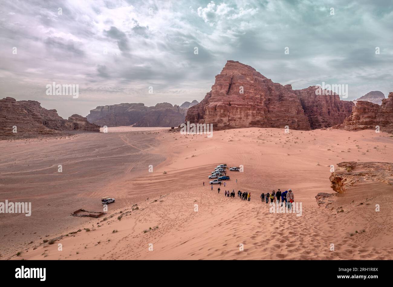 Touristen klettern eine Sanddüne unter dem dramatischen Himmel in Wadi Rum, Jordanien. Stockfoto