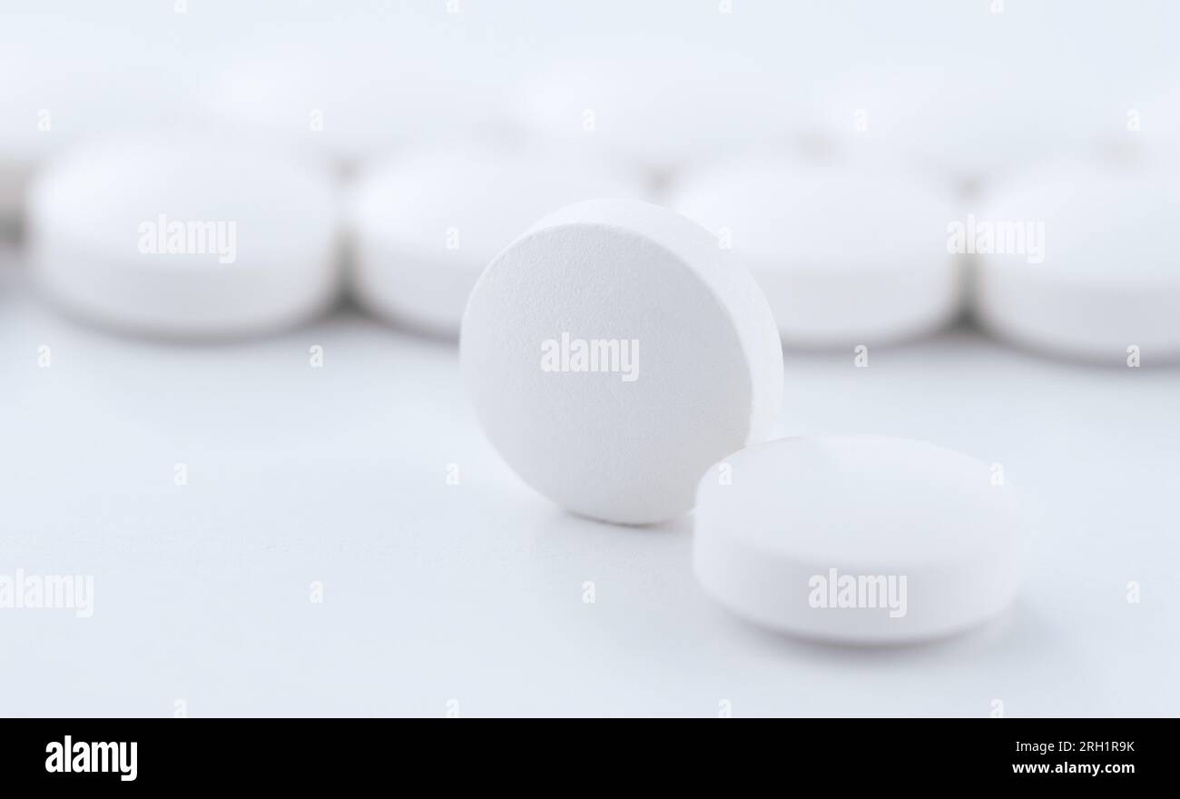 Nahaufnahme einer runden Pille vor dem Hintergrund von in einer Produktionslinie hintereinander gestapelten Tabletten. Stockfoto