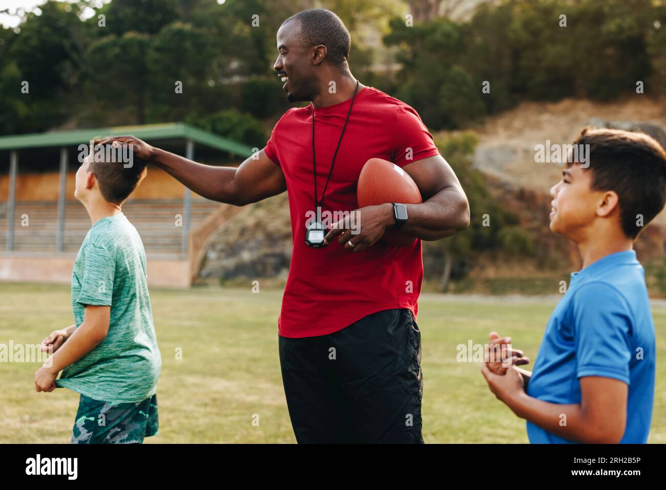 Der Trainer der Grundschule spielt American Football mit seinen Schülern. Sportlehrer, der eine Gruppe von Kindern in einer Schule ausbildet. Mentorenstudium Stockfoto