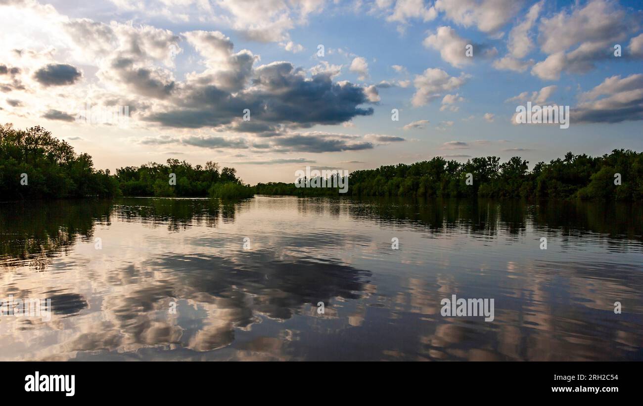 Die Landschaft des wolkigen Himmels bei Sonnenuntergang spiegelt sich im Wasser des Mississippi wider. Die von Bäumen gesäumten Ufer in der Nähe von Alton, IL Stockfoto
