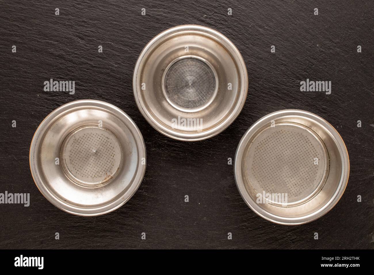Drei Metallsiebe für eine Kaffeemaschine auf einem Schieferstein, Makro, Draufsicht. Stockfoto
