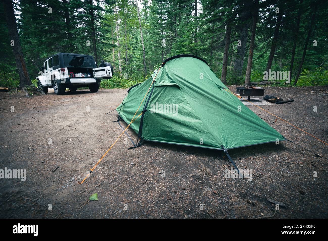 Ein kleines, grünes Zelt für zwei Personen befindet sich auf einem Campingplatz in der Nähe eines Geländewagens in einem Kiefernwald in Kanada Stockfoto