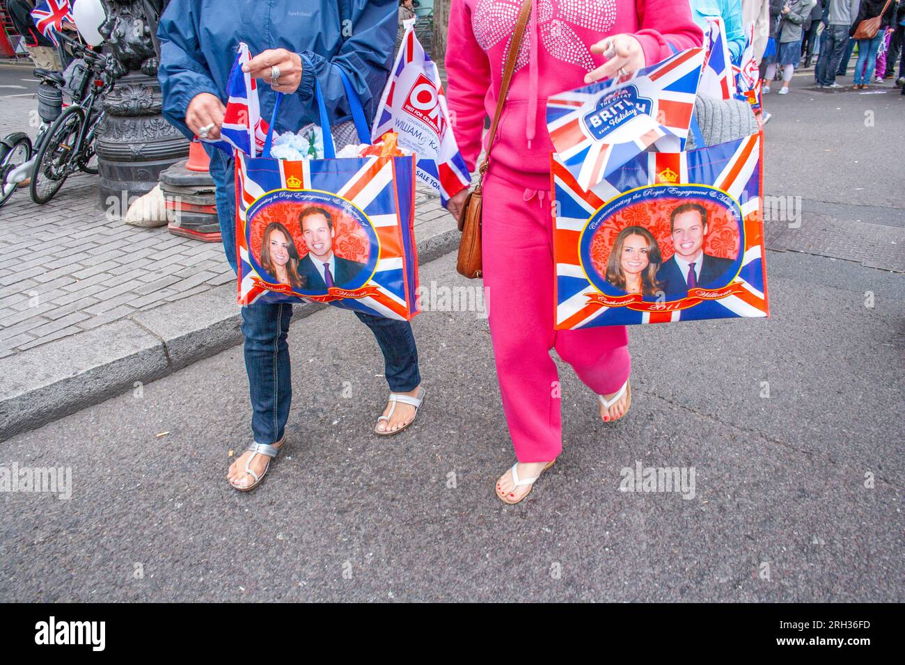 Zwei Personen gehen mit Taschen, die das Porträt von Catherine, Herzogin von Cambridge, und ihrem Ehemann Prinz William, London, Großbritannien zeigen Stockfoto