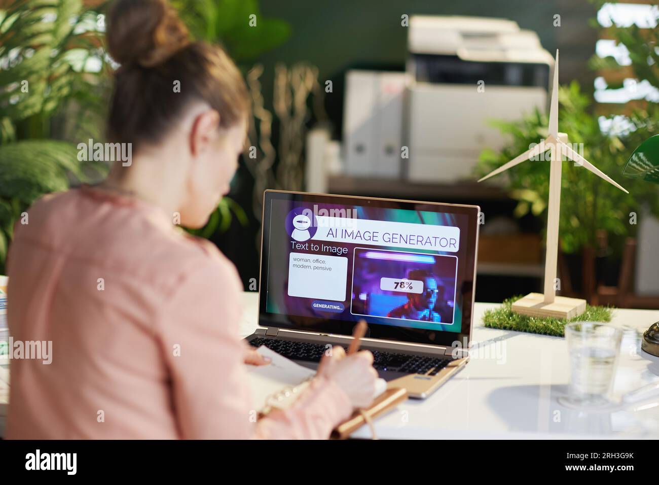 Von hinten gesehen: Moderne Geschäftsfrau mit Laptop, die Text-zu-Bild-Bildgenerator in einem modernen Büro verwendet. Stockfoto