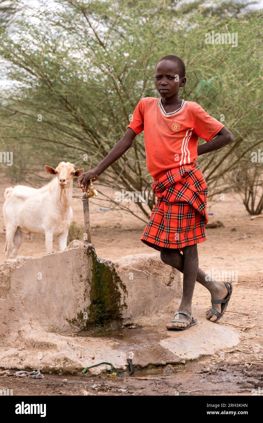 Ein junger kenianischer Junge steht an einem Wasserhahn, der frisches Wasser aus einem nahegelegenen Bohrloch, Baringo County, Kenia, bezieht Stockfoto