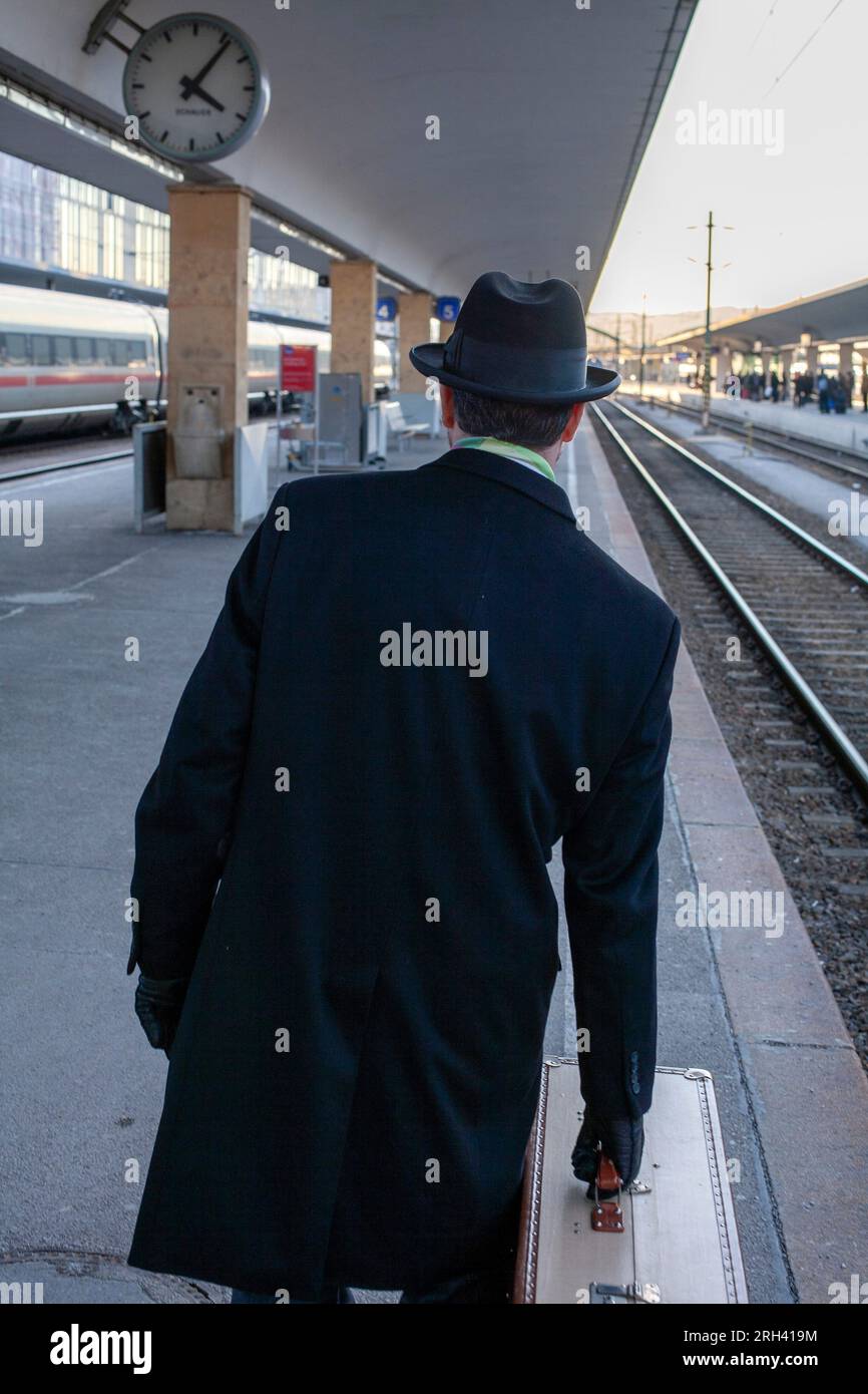 Ein Mann steht mit Koffern auf dem Bahnsteig und kümmert sich um die Ankunft des Zuges Stockfoto