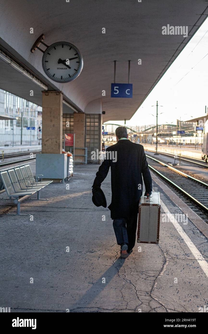 Ein Mann, der mit dem Koffer am Bahnhof spaziert. Ein Mann, der mit schwerem Koffer die Plattform runtergeht. Stockfoto