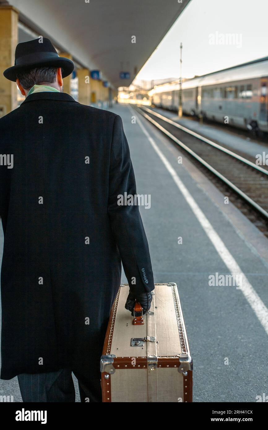 Ein Mann, der mit dem Koffer am Bahnhof spaziert. Ein Mann, der mit schwerem Koffer die Plattform runtergeht. Stockfoto