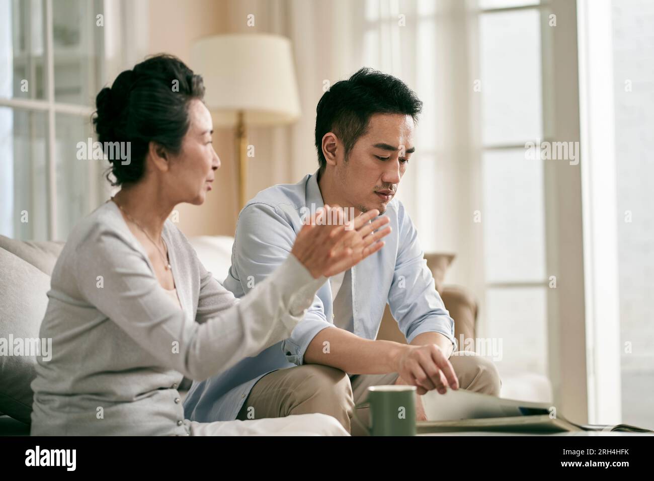 Ältere asiatische Mutter und erwachsener Sohn sitzen auf der Couch im Wohnzimmer zu Hause und unterhalten sich Stockfoto