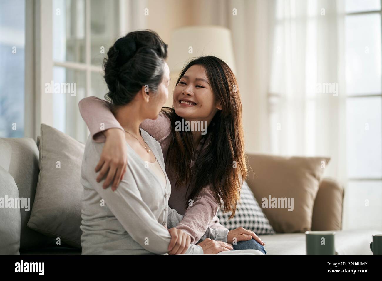 asiatische Erwachsene Tochter und Seniorenmutter, die zu Hause auf der Couch sitzen und ein angenehmes Gespräch führen Stockfoto