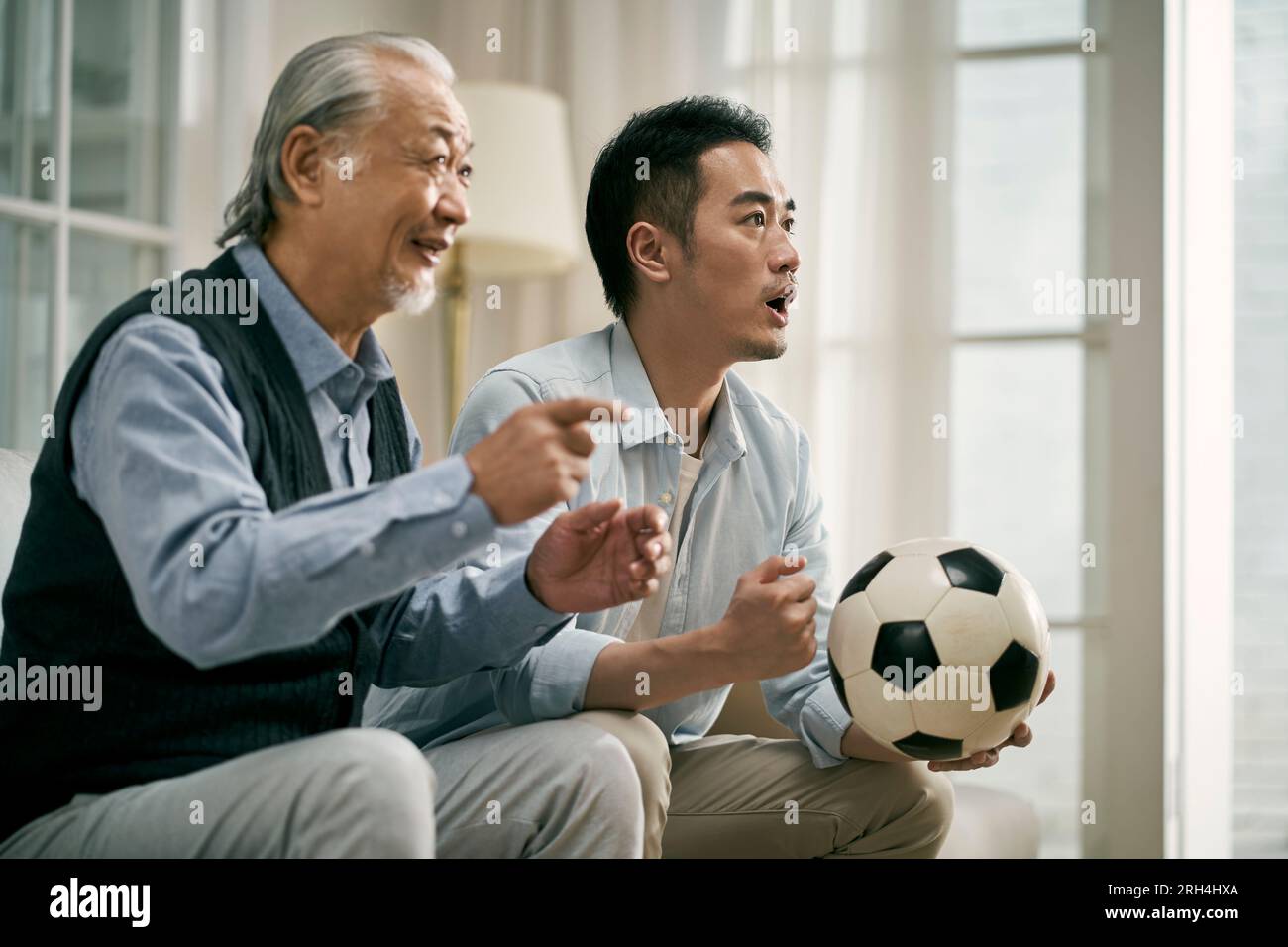 asiatischer Seniorenvater und erwachsener Sohn, die zusammen ein Fußballspiel im fernsehen sehen Stockfoto