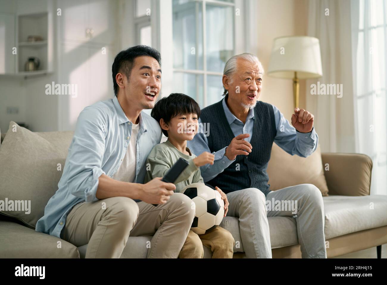 asiatischer Vater Großvater, der zu Hause auf der Couch sitzt und zusammen live das Fußballspiel im Fernsehen ansieht Stockfoto