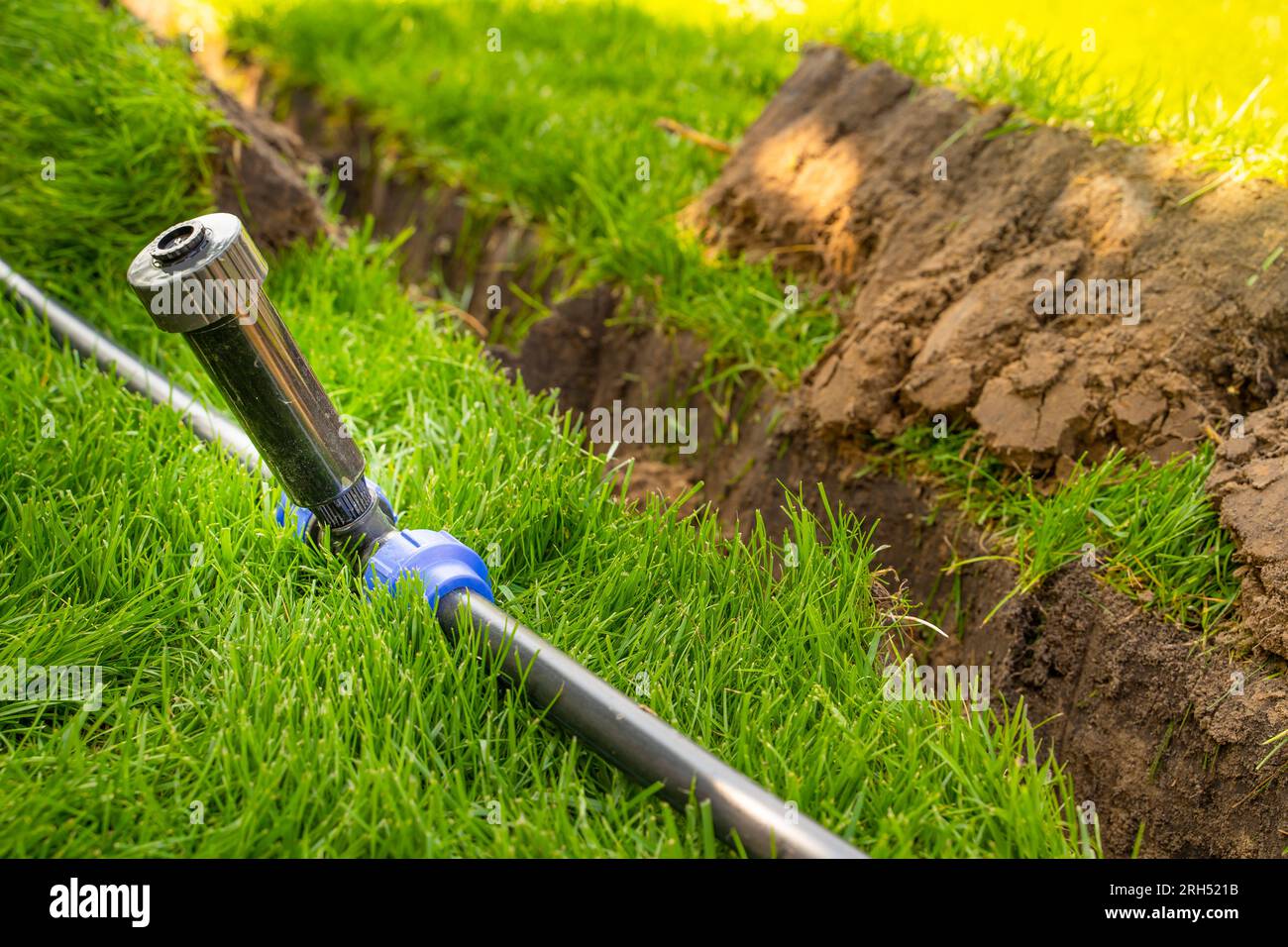 Selbstinstallation der Bewässerung mit einem einziehbaren Sprinkler im fertiggestellten Rasen. Verlegung von Wasserrohren mit Sprühgeräten unter dem Rasen zur Bewässerung. Stockfoto