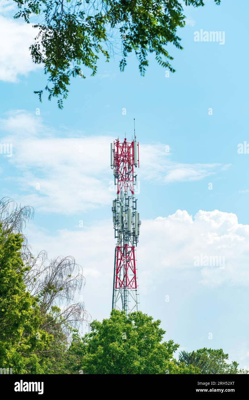 Mobilfunk-Basisstation-Pylon mit Antennen und anderen Telekommunikationsgeräten, die durch Parkbäume gesehen werden Stockfoto