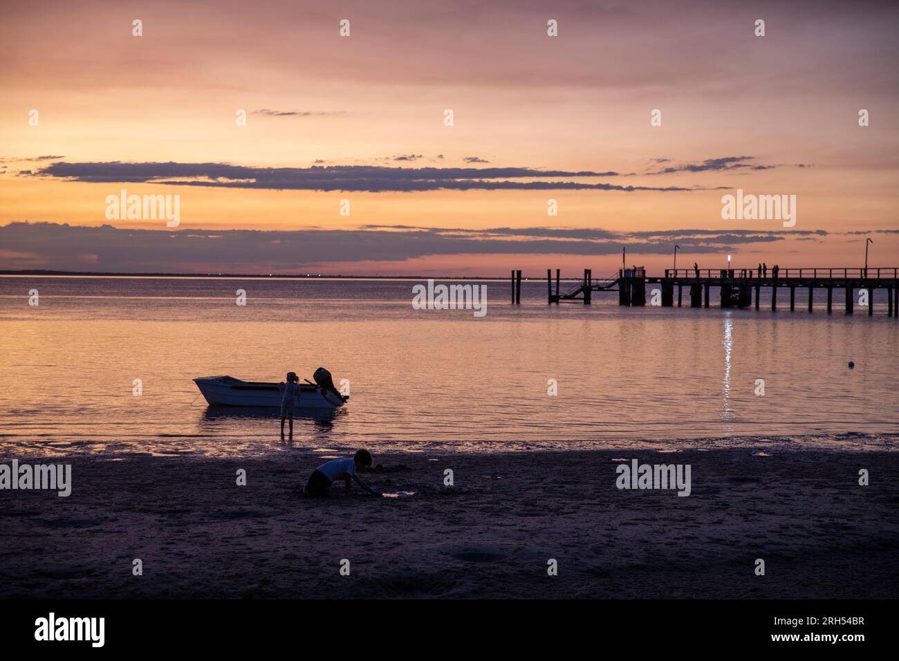 Fraser Island K'gari Sonnenuntergang über kingfisher Bay und Coral Sea mit Silhouetten Boot, Person und Fähre Pier, Queensland, Australien Stockfoto
