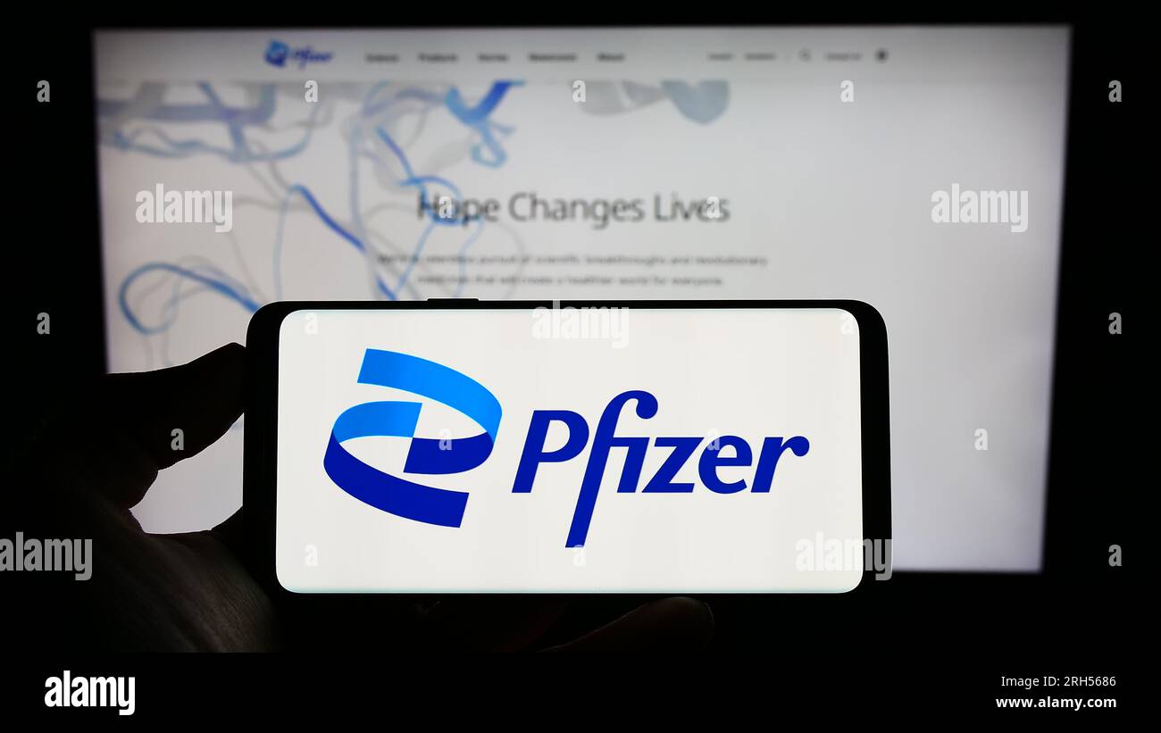 Person, die ein Mobiltelefon mit dem Logo des US-amerikanischen Pharmaunternehmens Pfizer Inc. Auf dem Bildschirm vor der Unternehmenswebseite hält. Konzentrieren Sie sich auf das Display des Telefons. Stockfoto