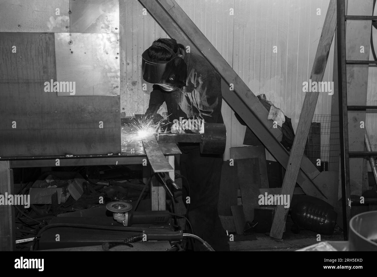 Ein männlicher Arbeiter in Uniform, der am Arbeitsplatz in der Fabrik ein Metallteil mit einem Schneidwerkzeug schneidet. Funken, Flammen und Rauch beim Schneiden von Metallteilen. Cuttin Stockfoto