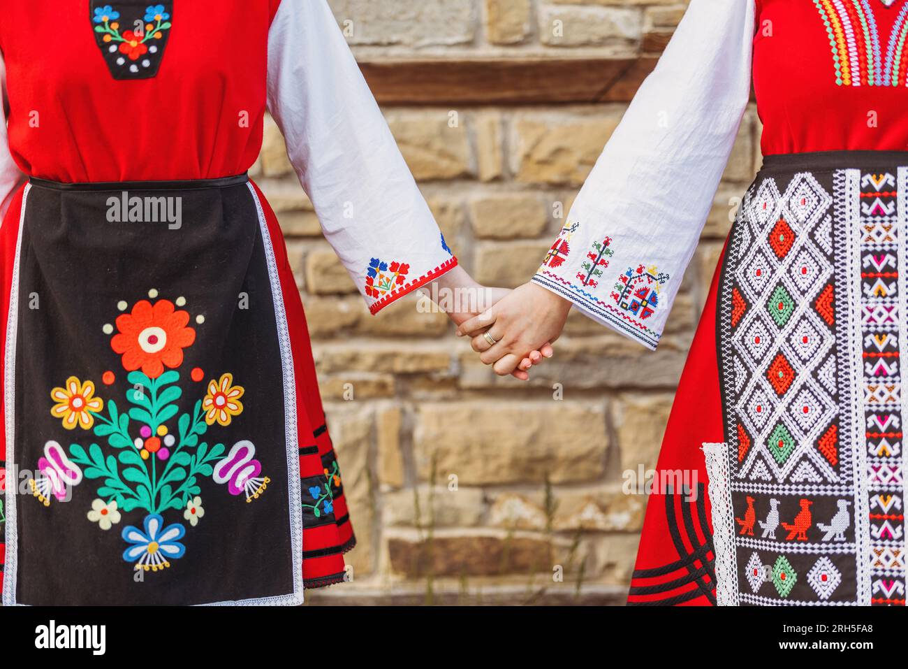 Mädchen in traditionellen bulgarischen ethnischen Kostümen mit folkloristischer Stickerei, die Händchen hält. Der Geist Bulgariens - Kultur, Geschichte und Traditionen. Stockfoto