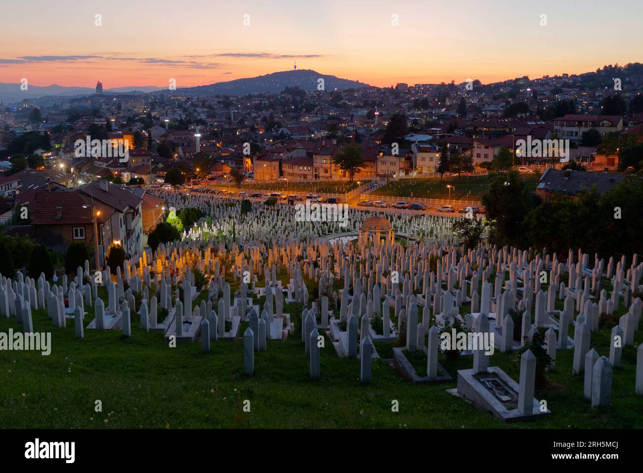 Friedhof bei Nacht mit Häusern auf dem Hügel dahinter in Sarajevo, Bosnien und Herzegowina, 13. August 2023. Stockfoto