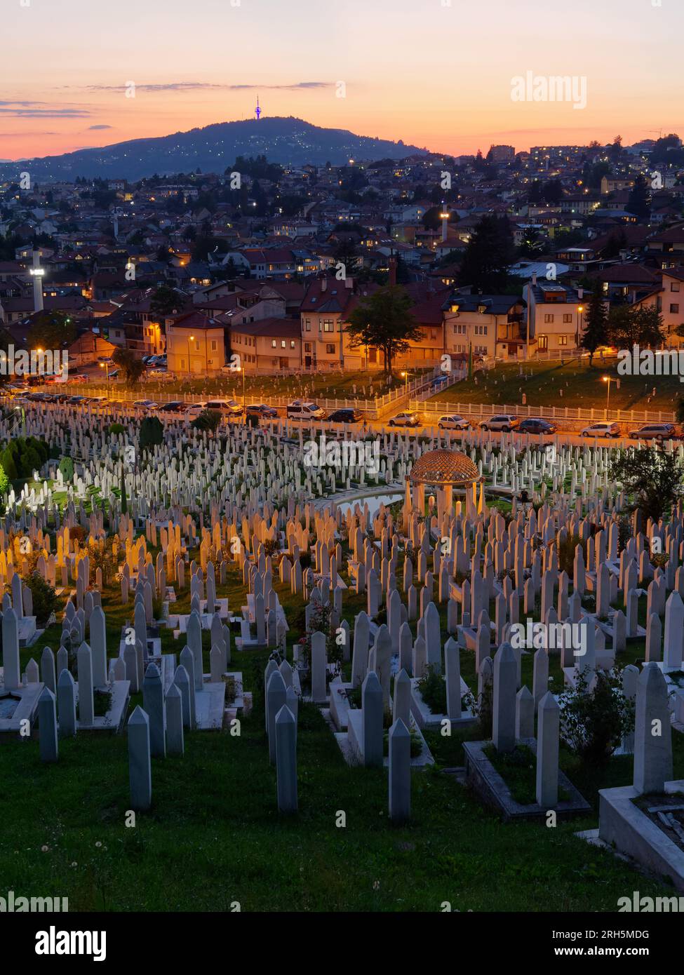 Friedhof bei Nacht mit Häusern auf dem Hügel dahinter in Sarajevo, Bosnien und Herzegowina, 13. August 2023. Stockfoto