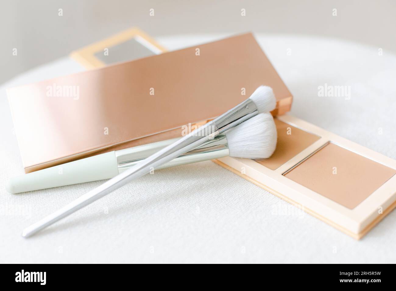 Make-up-Bürsten, Puder, Augenschatten und Rouge auf einem Leinenhocker Stockfoto