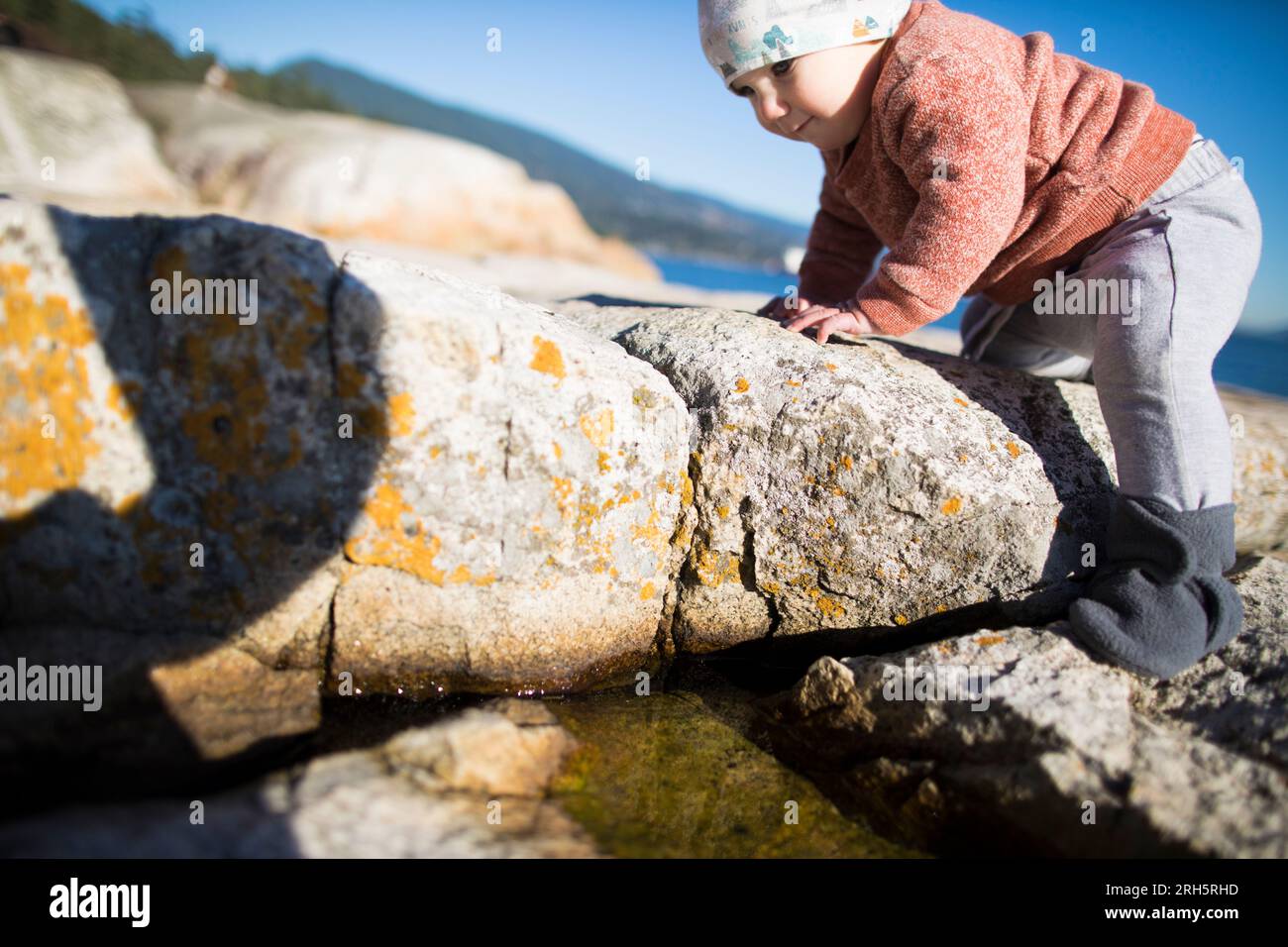 Baby klettert draußen am Strand auf Felsen. Stockfoto
