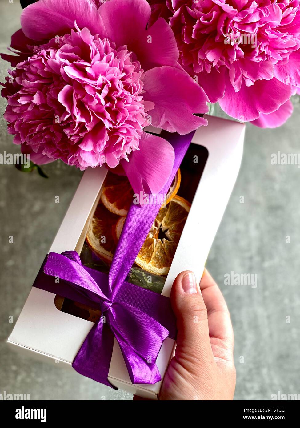 Hand mit einem Geschenk auf dem Hintergrund von Pfingstrosen Stockfoto