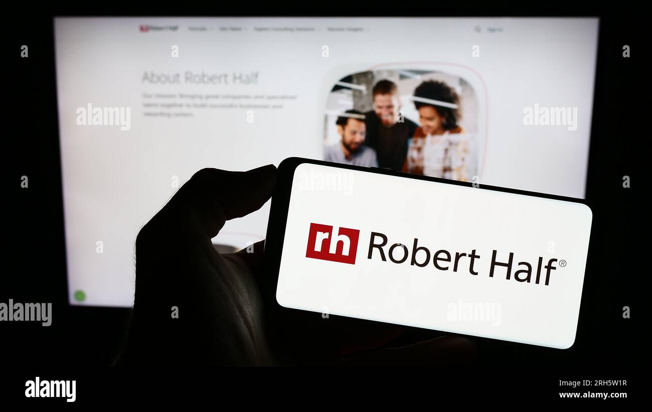 Person, die ein Mobiltelefon mit dem Logo des amerikanischen Unternehmens Robert Half International Inc. Auf dem Bildschirm vor der Webseite hält. Konzentrieren Sie sich auf das Display des Telefons. Stockfoto