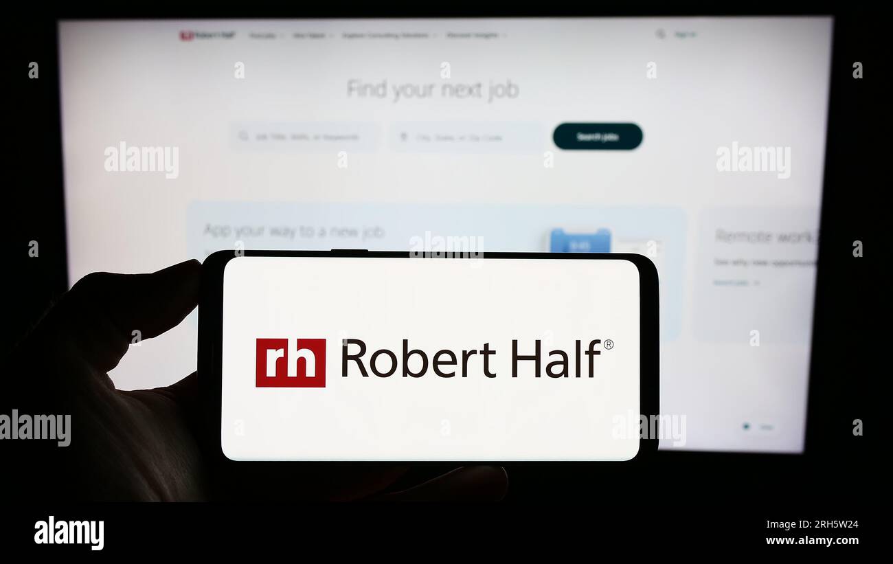 Person, die ein Mobiltelefon mit dem Logo der US-amerikanischen Firma Robert Half International Inc. Auf dem Bildschirm vor der Unternehmenswebseite hält. Konzentrieren Sie sich auf das Display des Telefons. Stockfoto