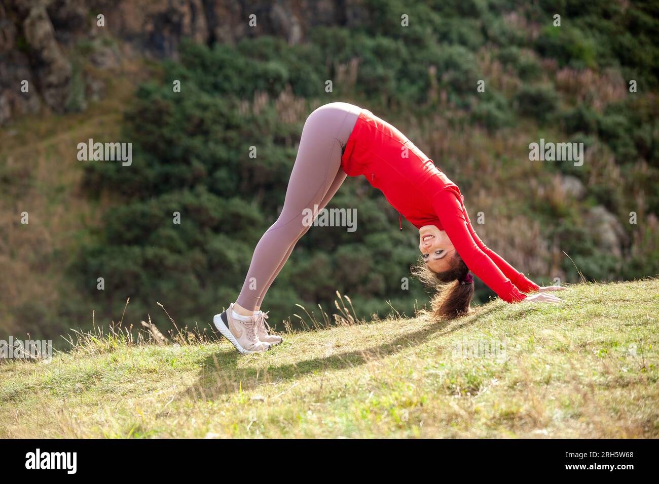 Eine junge Frau mit Leggings, die in einem öffentlichen Park in Edinburgh das Hundeyoga-Stretch nach unten vorführt Stockfoto