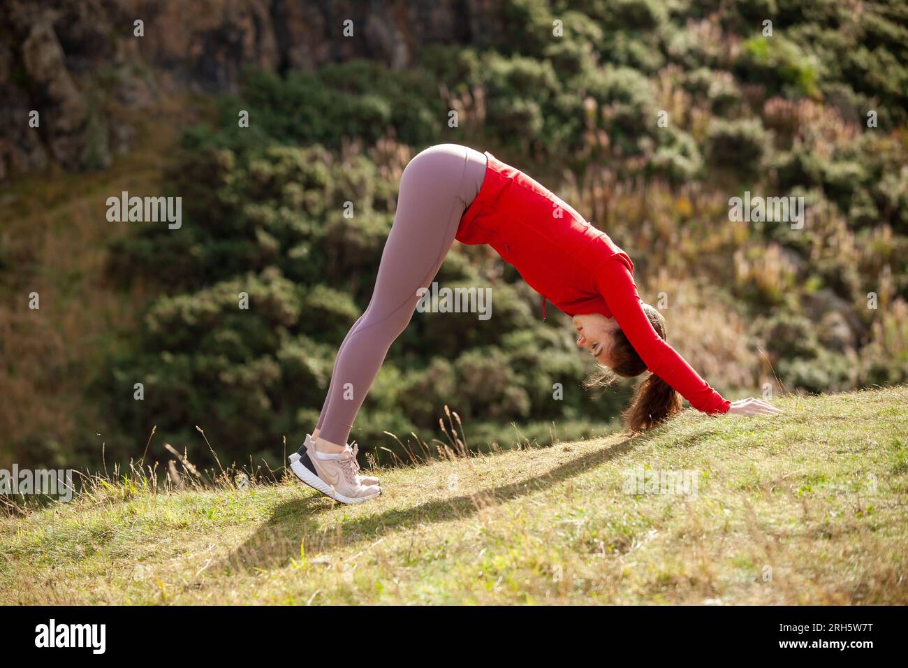 Eine junge Frau mit Leggings, die in einem öffentlichen Park in Edinburgh das Hundeyoga-Stretch nach unten vorführt Stockfoto