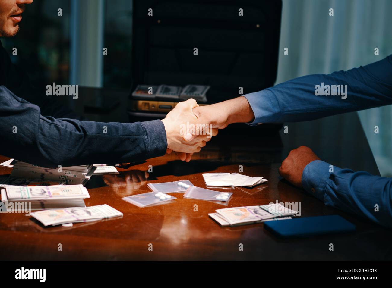 Zugeschnittenes Bild eines Drogenhändlers und Käufers, der die Hände über den Tisch schüttelt, mit Geld und kleinen Taschen mit Tablets Stockfoto