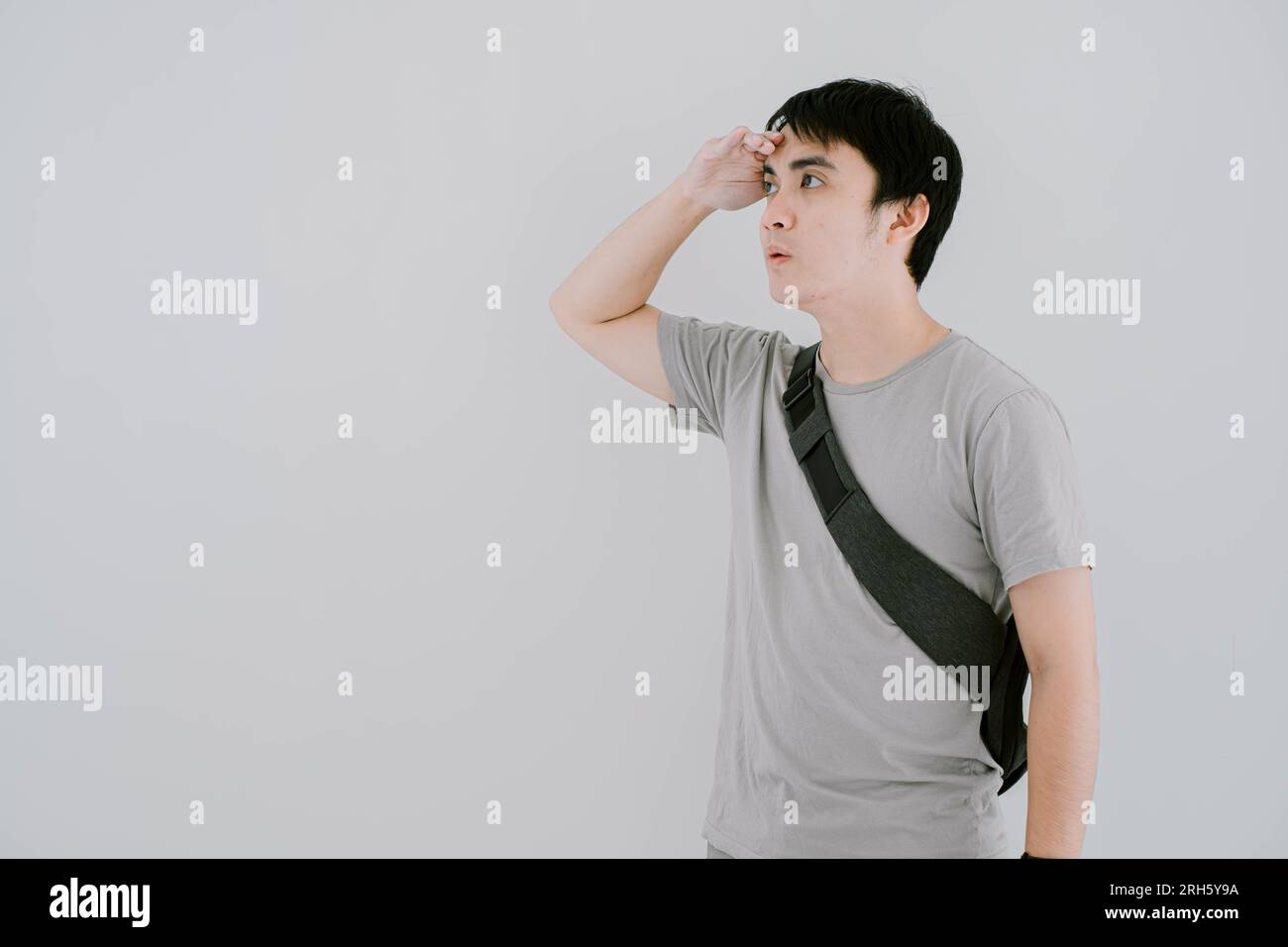 Die selektive Fokusaufnahme eines jungen asiatischen Mannes, der ein lässiges, salbeigrünes T-Shirt, eine Smartwatch und eine minimalistische Tragetasche trägt, blickt weit weg Stockfoto