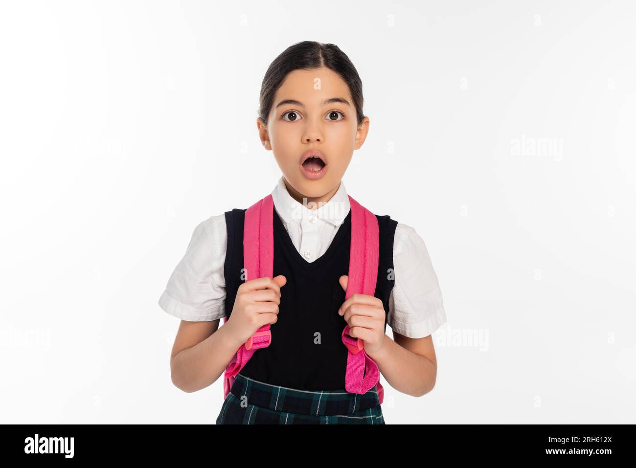 Neues Schuljahr, schockiertes Mädchen mit Rucksack, das auf die Kamera schaut, isoliert auf Weiß, Schülerin in Uniform Stockfoto