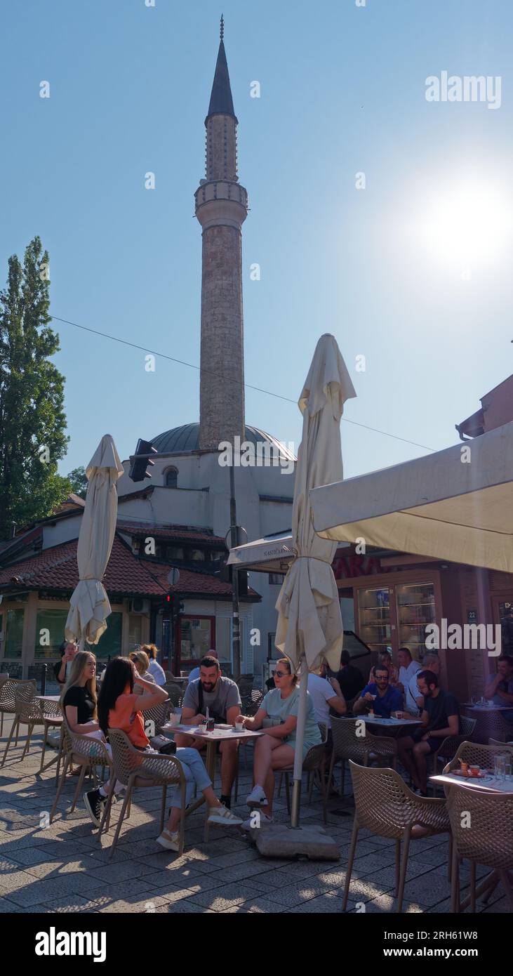 Gäste in einem Café/Restaurant mit einem Minarett im Stadtteil Baščaršija in Sarajevo, Bosnien und Herzegowina, 14. August 2023. Stockfoto