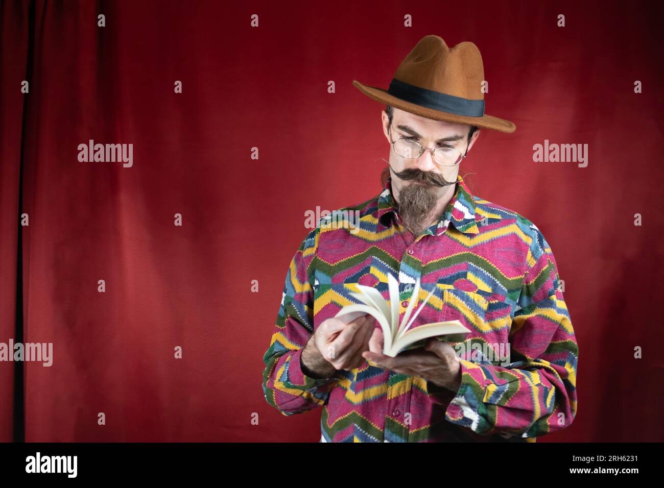 Ein alter Hipster-Mann mit Brille, Hut und Schnurrbart, der sich ein Buch ansieht Stockfoto